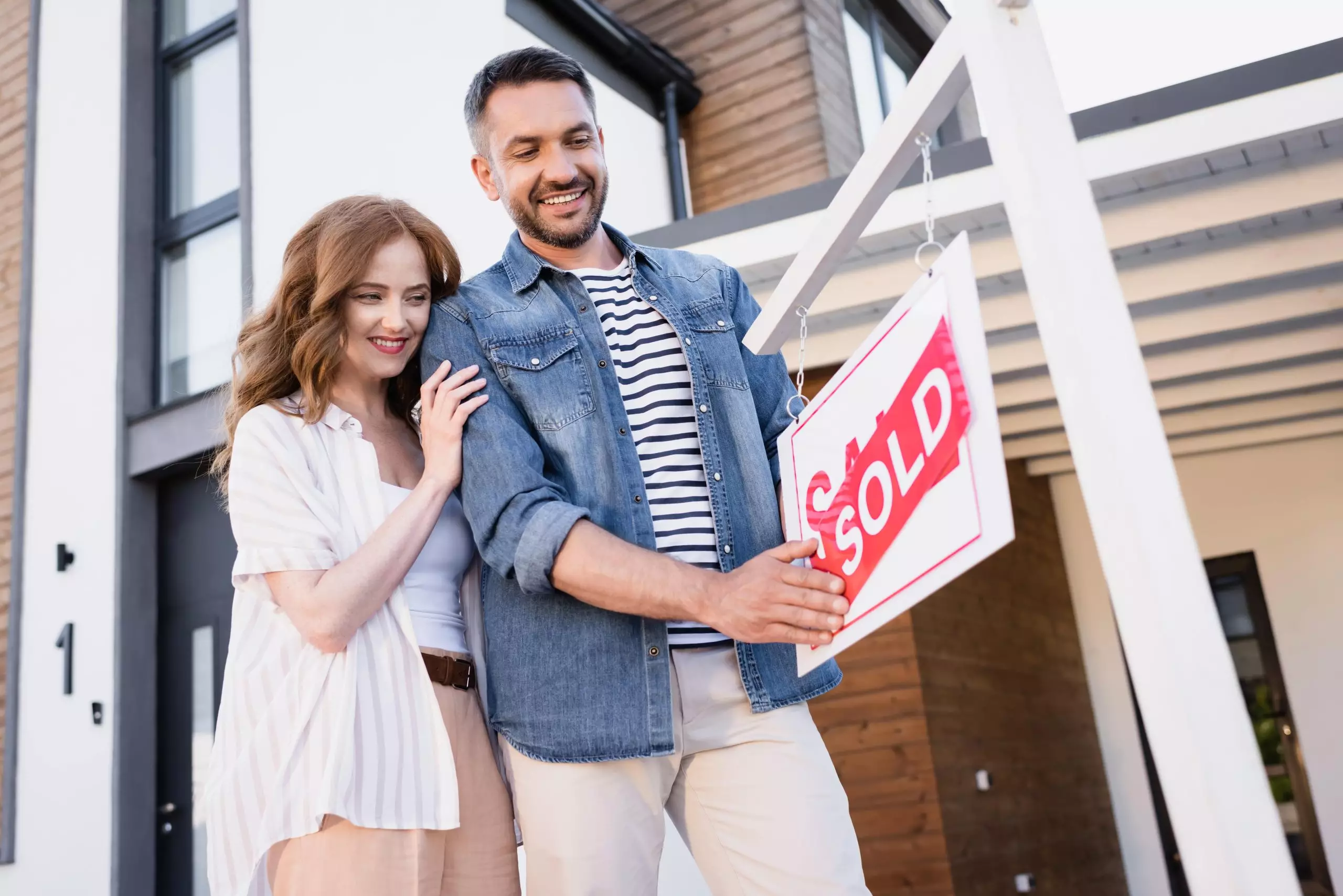 Smiling couple looking at house for sale sign